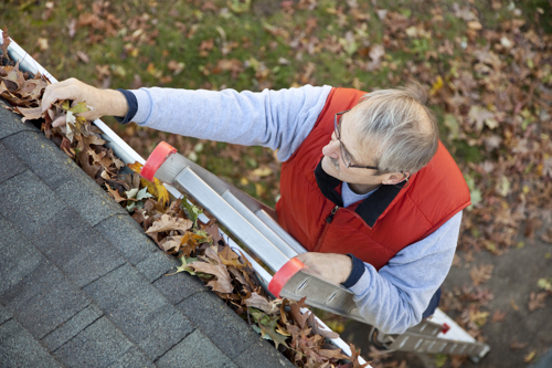 Senior man cleaning leafs out of gutter.