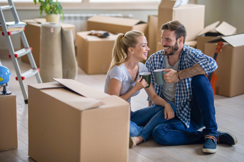 couple chatting and drinking tea surrounded with cardboard boxes for moving homes